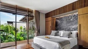 A modern bedroom with a large bed, wooden headboard, and a view of lush greenery. - Villa Na (Bali)
