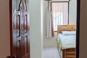 A bedroom with a wooden bed, a window with curtains, and a door.