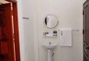 Een badkamer met een wit wastafel, een ronde spiegel en een handdoek aan een rek.