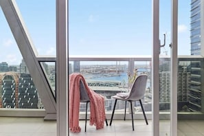 Un balcón con vistas a un puente y edificios, una silla con una manta y una puerta de cristal.