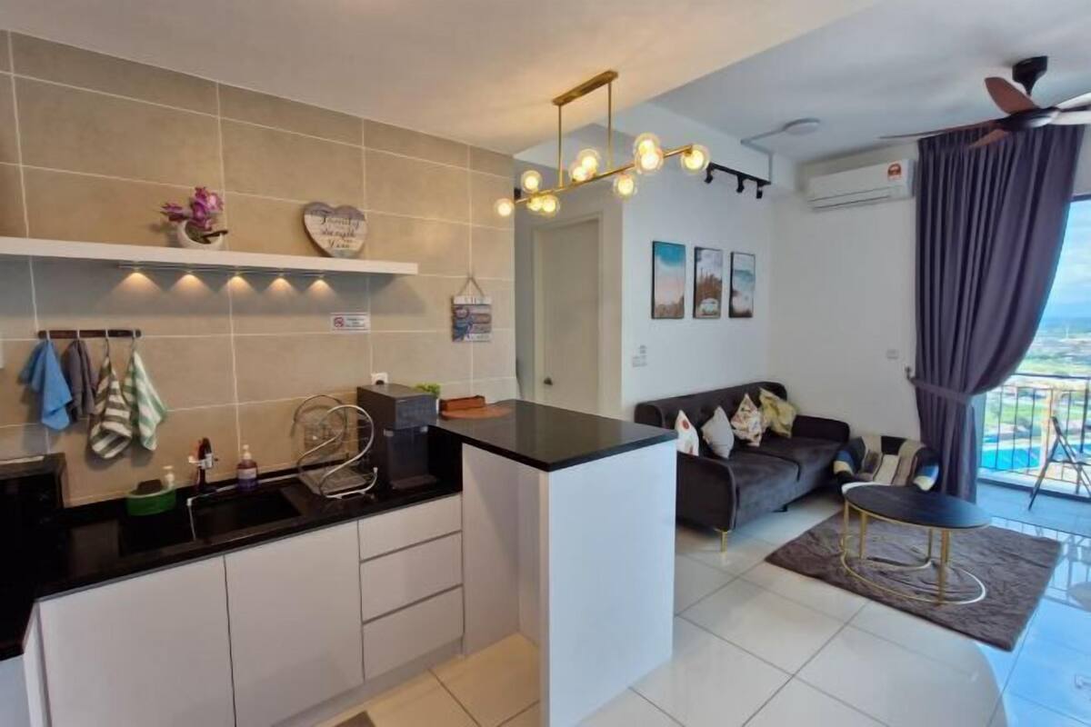 A modern kitchen with a black countertop, white cabinets, and a built-in island. There is a dining area with a black table and a sofa. The room has a large window with a view of the outdoors.