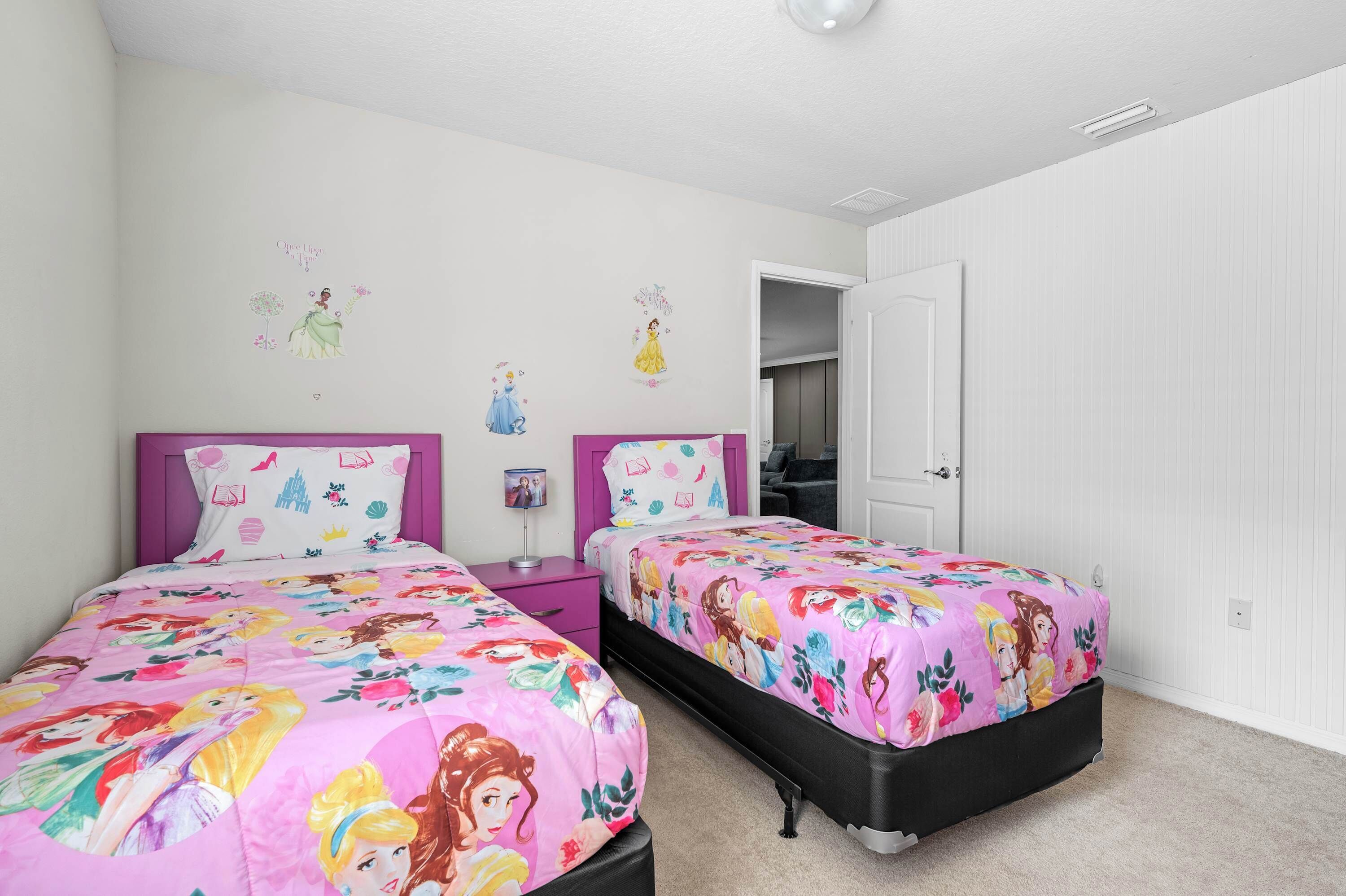 A bedroom with two beds, white walls, and a door leading to another room.