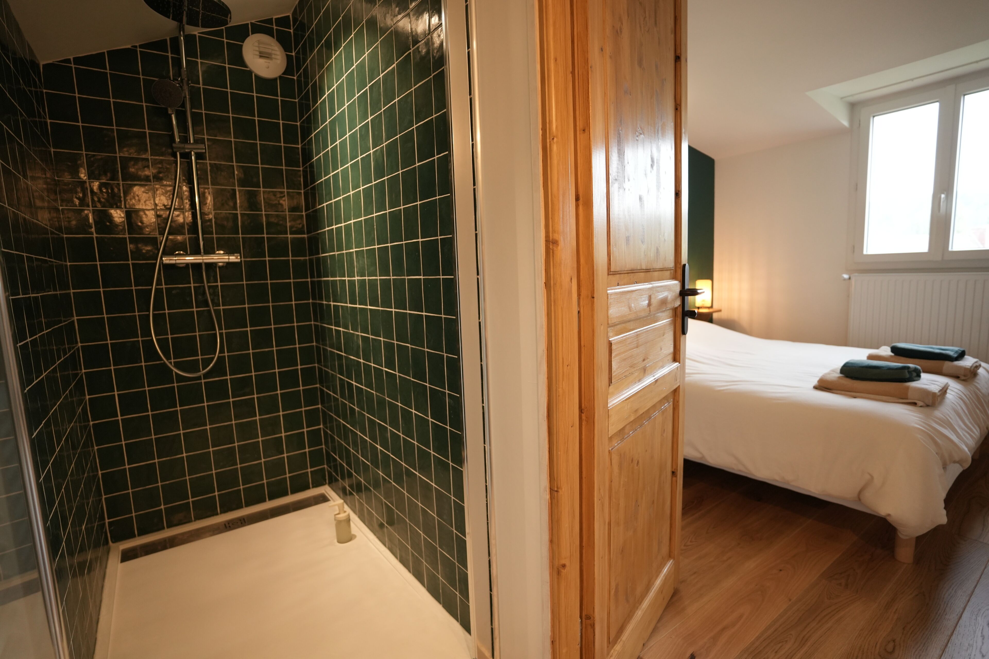 A bathroom with a shower, a bed with a wooden headboard, and a window with daylight.