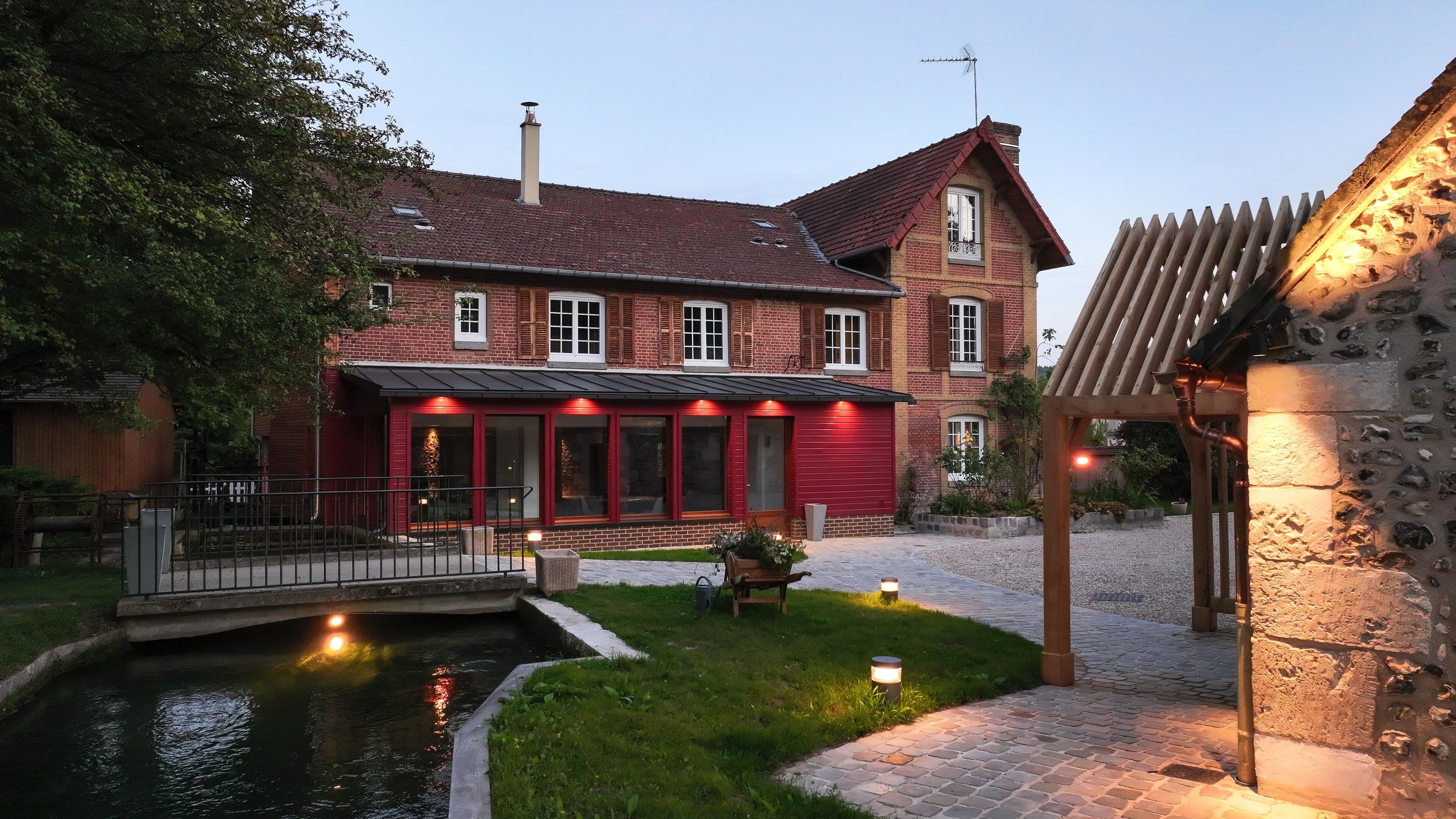 A large brick house with a red facade, a small pond, and a stone structure.
