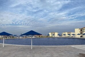 A waterfront area with a pool, umbrellas, and buildings in the background. - Albatros Makadi Resort - 24 HRS All Inclusive (Hurghada)