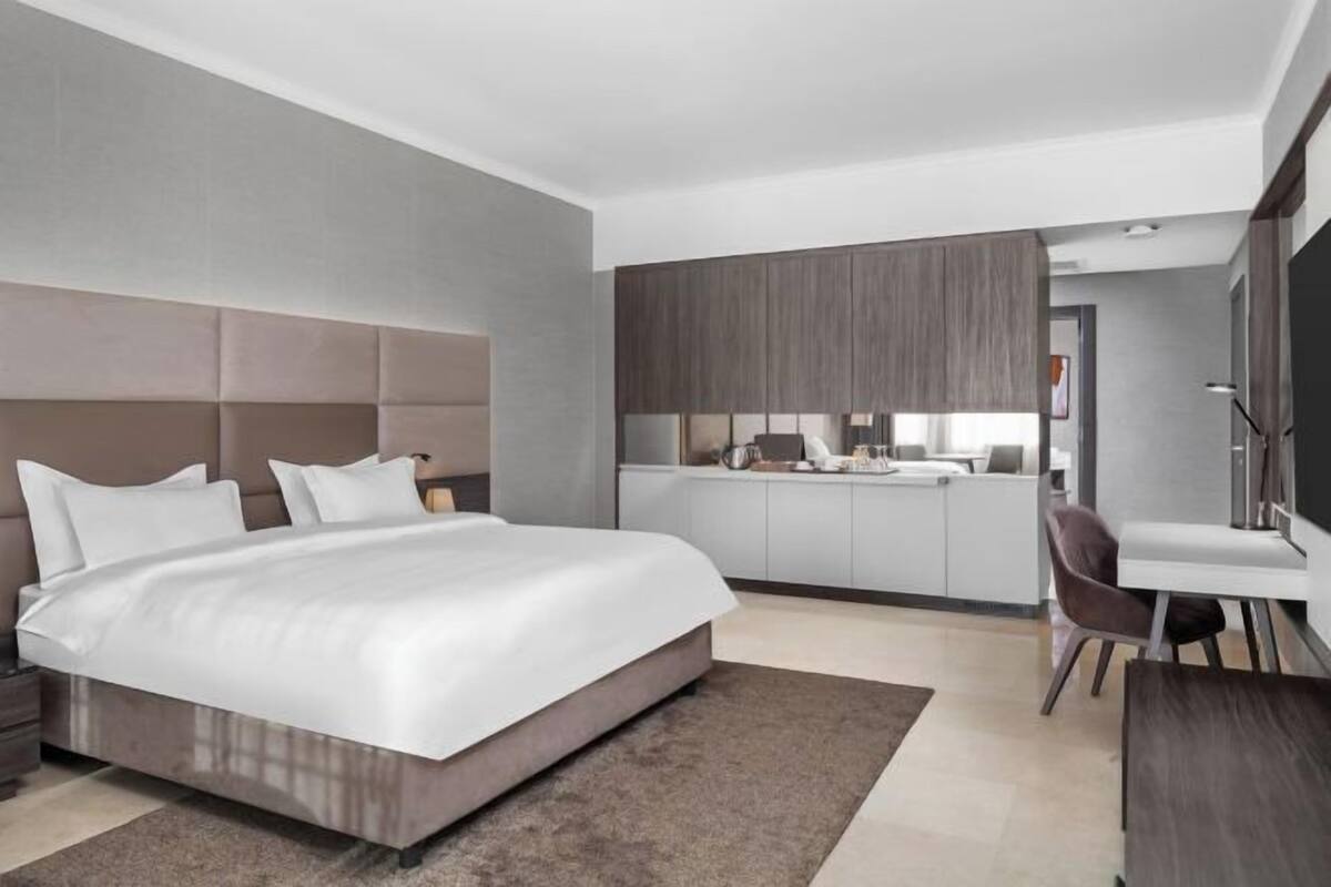 Ein modernes Schlafzimmer mit einem großen Bett, einem Schreibtisch und einer kleinen Küchenzeile im Hintergrund.