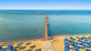 Een strand met een pier die het water in reikt, zandstrand met parasols en een heldere lucht.