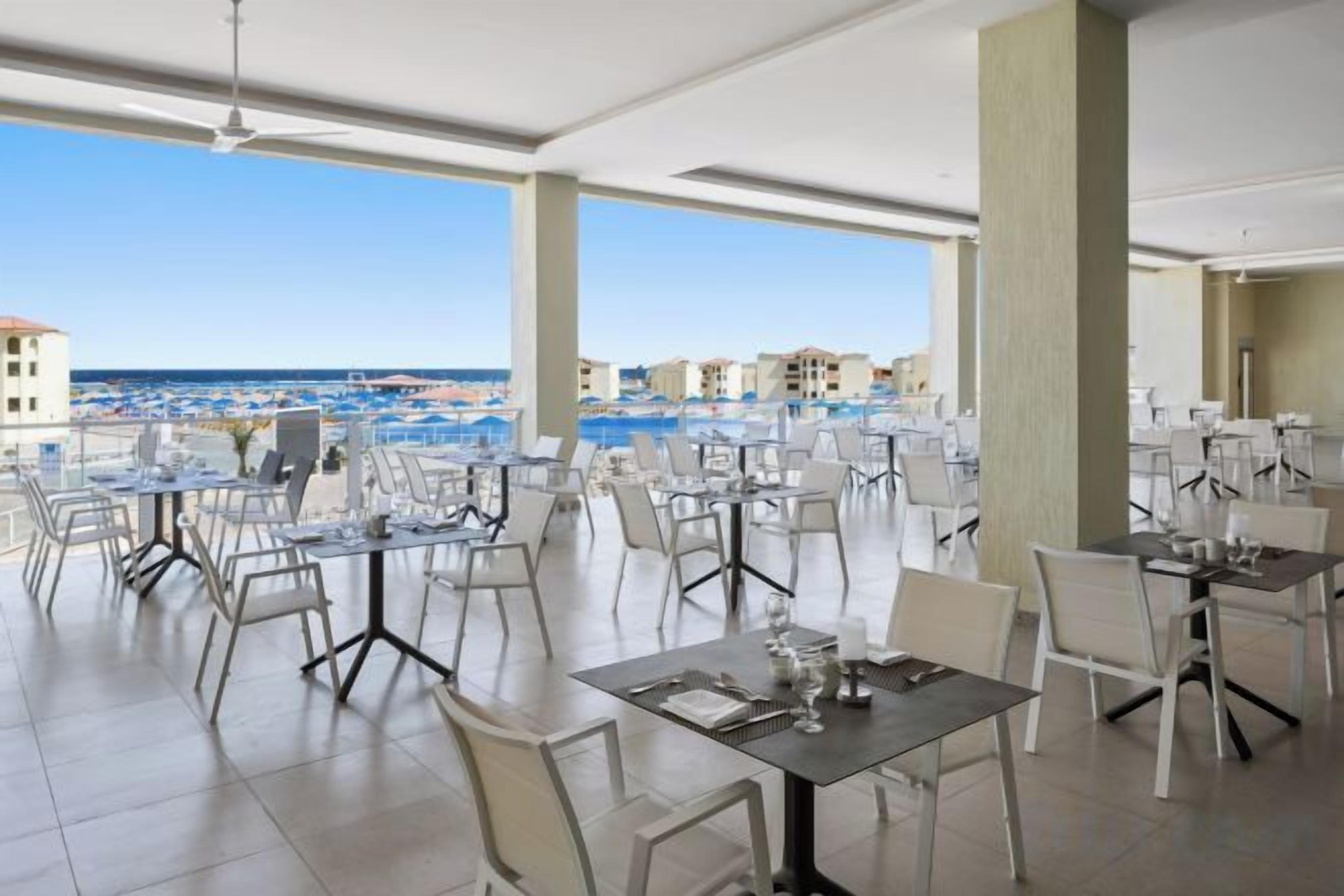 An outdoor dining area with tables and chairs, overlooking a beach and ocean.