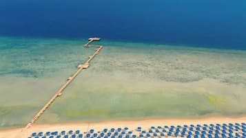 Ein Strand mit einer hölzernen Steg, der sich ins Wasser erstreckt, einer Reihe von Sonnenschirmen und freiem Blick auf den Ozean.