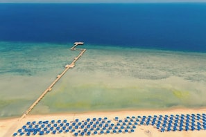 A beach with a wooden jetty extending into the water, a row of umbrellas, and a clear view of the ocean. - Albatros Makadi Resort - 24 HRS All Inclusive (Hurghada)