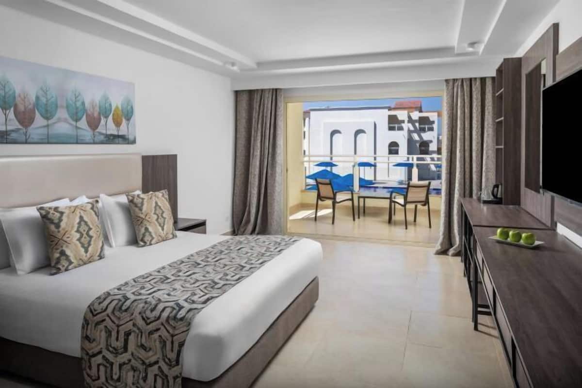 Ein Hotelzimmer mit Bett, Fernseher, Essbereich mit Tisch und Stühlen sowie Blick ins Freie.