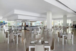 A spacious indoor dining area with multiple tables and chairs, a central bar area, and large windows allowing natural light. - Albatros Makadi Resort - 24 HRS All Inclusive (Hurghada)
