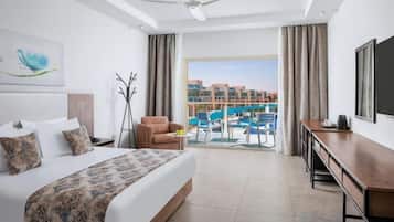Quarto de hotel com cama, escrivaninha, cadeira, varanda com vista para a piscina e paisagem urbana ao fundo.