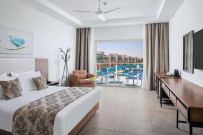Ein Hotelzimmer mit Bett, Schreibtisch, Stuhl, einem Balkon mit Blick auf den Pool und einer Stadtansicht im Hintergrund.