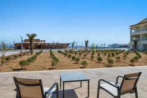 A beachfront patio with outdoor seating, a sandy area with small plants, and a building in the background. - Albatros Makadi Resort - 24 HRS All Inclusive (Hurghada)