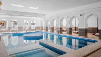 A swimming pool with a clear blue water surface, surrounded by white walls with arches and a tiled floor.