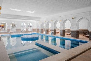 Ein Schwimmbecken mit klar blauem Wasser, umgeben von weißen Mauern mit Bögen und einem gefliesten Boden.