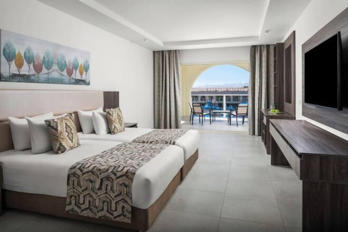 Ein Hotelzimmer mit Bett, Fernseher, Schreibtisch und einem Balkon mit Blick.