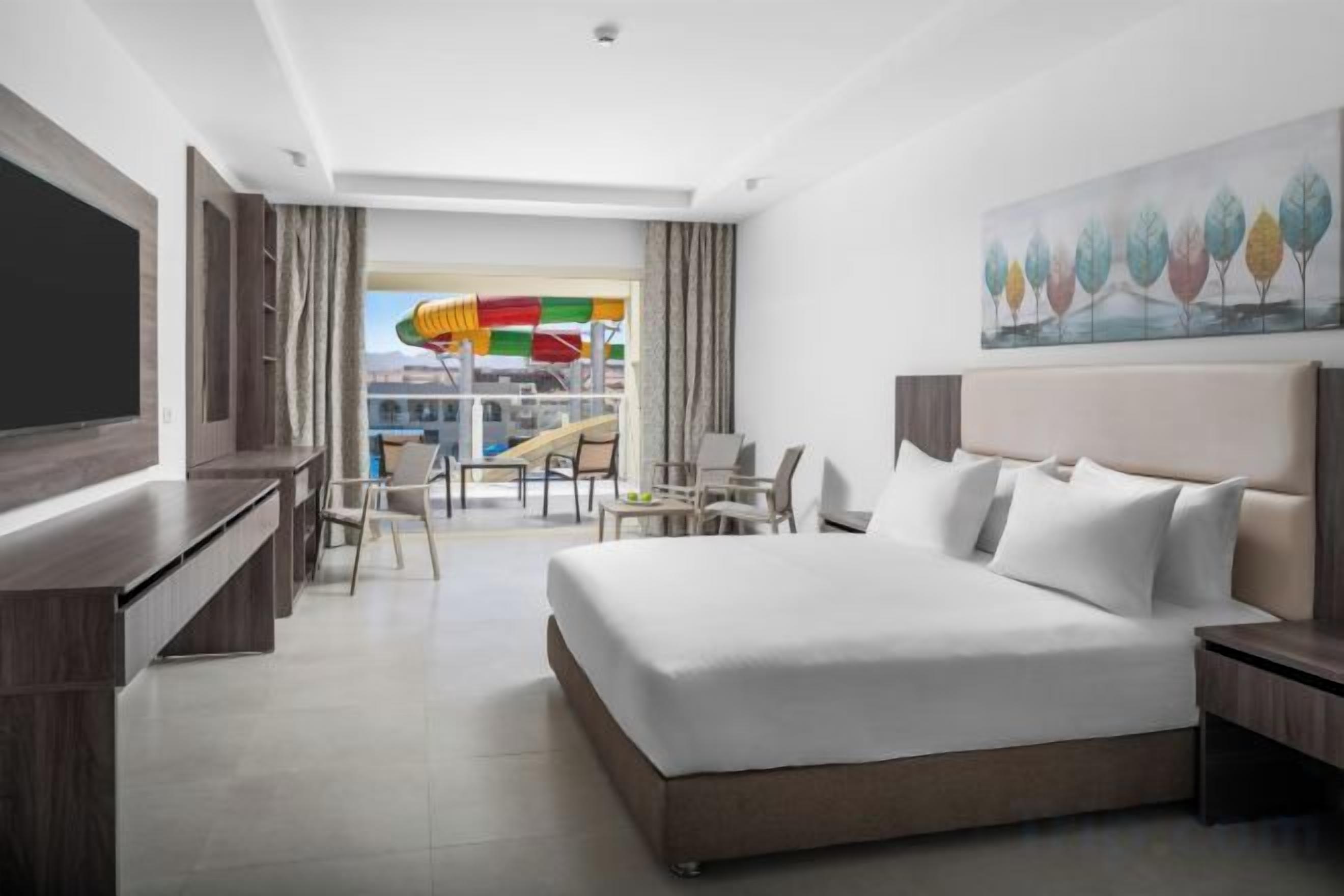 A hotel room with a bed, a desk, a chair, a TV, and a balcony with a view of a water slide.