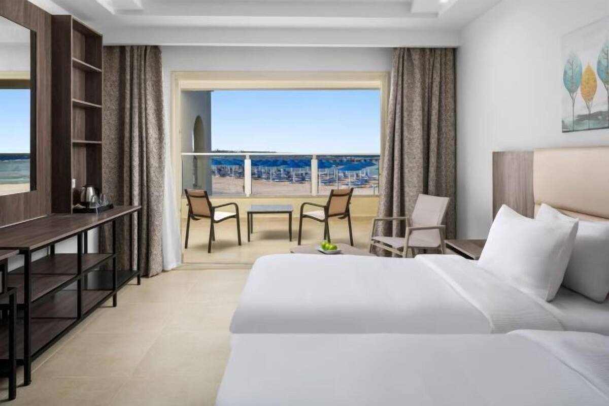Ein Hotelzimmer mit einem großen Bett, einem Schreibtisch und einem Balkon mit Stühlen.