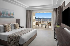 A hotel room with a bed, a TV, a balcony with a table and chairs, and a view of the sea. - Albatros Makadi Resort - 24 HRS All Inclusive (Hurghada)
