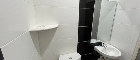 Un baño pequeño con azulejos blancos, un inodoro, un lavamanos y un espejo.