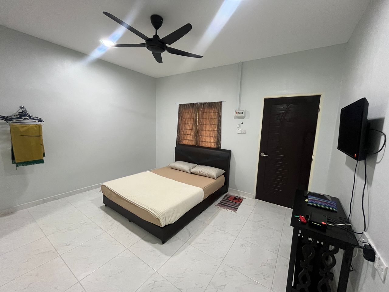A bedroom with a bed, a ceiling fan, a TV, and a door.