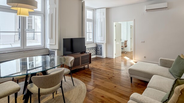 A modern living room with a glass dining table, comfortable seating, a flat-screen TV, and a large window providing natural light. - Bairro Alto Garden by Homing (Lisbon)