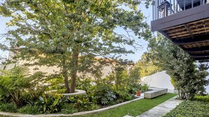A landscaped garden area with a variety of plants and a tree, a concrete pathway, and a modern building structure in the background. - Bairro Alto Garden by Homing (Lisbon)