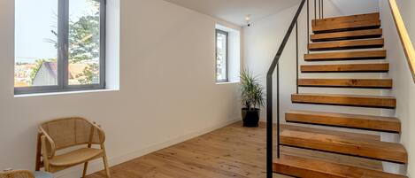 A spacious room with a wooden staircase, large windows, and a potted plant.