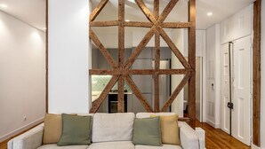 A modern living room with a grey sofa, wooden beams, and white walls. - Bairro Alto Garden by Homing (Lisbon)