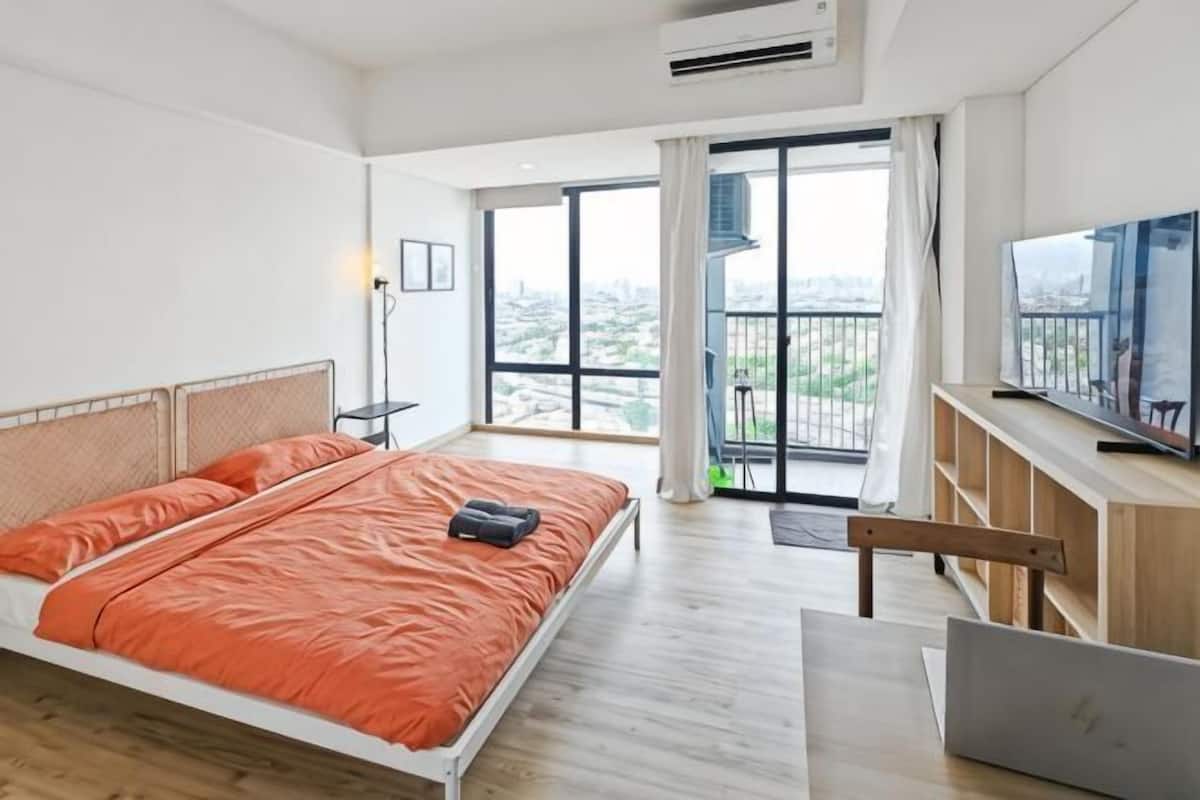 A modern hotel room with a large bed, a desk, a laptop, and a TV.