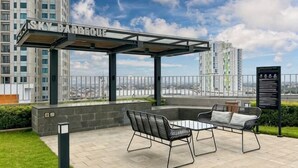 A covered outdoor seating area with a view of a cityscape, a sign reading 'SKY BARBEQUE,' and a black information board. - Newly Studio Apt w/ Pool, Gym Netflix (South Jakarta)