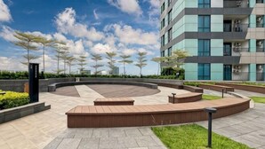 A landscaped courtyard with a circular seating area, surrounded by a modern building with balconies. - Newly Studio Apt w/ Pool, Gym Netflix (South Jakarta)