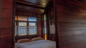 Ein Zimmer in einer Holzhütte mit einem Bett, einem Vorhangfenster und einer Holzdielendecke.