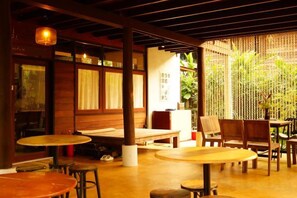 An indoor seating area with tables and chairs, wooden beams, and a plant in the background. - Lanna Localstay (San Kamphaeng)