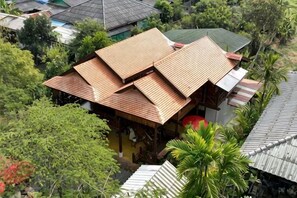 A traditional house with a sloped roof, surrounded by lush greenery and other residential buildings. - Lanna Localstay (San Kamphaeng)