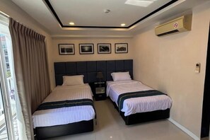 Une chambre d’hôtel avec deux lits, une tête de lit, une table de chevet et une fenêtre avec des rideaux.