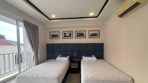 A hotel room with two beds, a dark headboard, a window with curtains, and framed pictures on the wall. - New Nordic Club 1 Condotel South Pattaya Twin Standard Room (Pattaya)