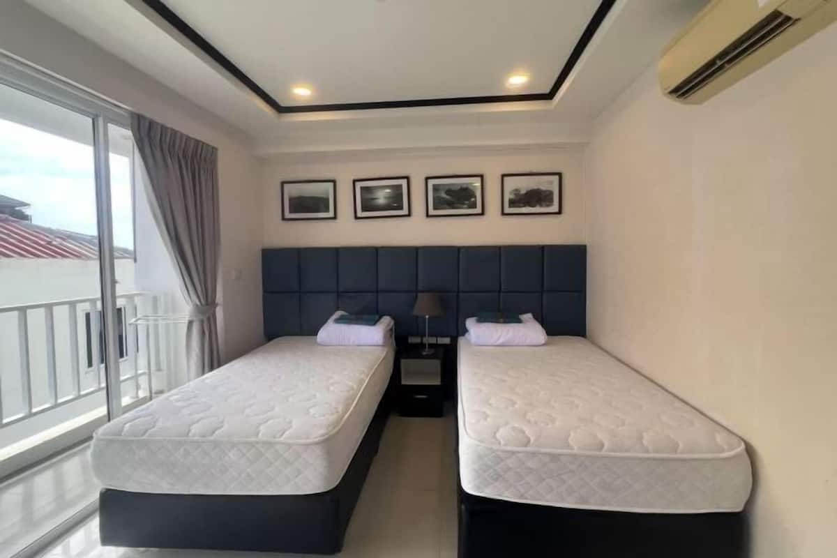 Ein Hotelzimmer mit zwei Betten, einem dunklen Kopfteil, einem Fenster mit Vorhängen und gerahmten Bildern an der Wand.