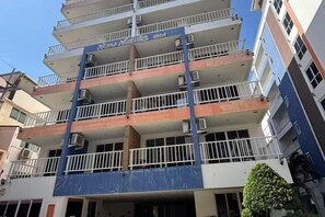 Un immeuble à plusieurs étages doté de balcons, de climatiseurs et d’un auvent bleu.