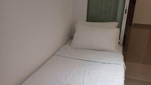 A small, single-bed room with white bedding and a window with a green curtain. - Urban Retreat @ The Shore • CBD • Pool (Kota Kinabalu)