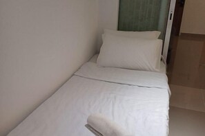 A small, single-bed room with white bedding and a window with a green curtain.