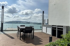 A wooden deck with a table and chairs, overlooking a body of water and a distant shoreline. - Urban Retreat @ The Shore • CBD • Pool (Kota Kinabalu)