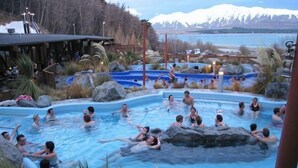 A pool area with people swimming and relaxing, surrounded by rocks and plants. - Alpine Star (Lake Tekapo)