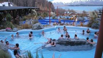 A pool area with people swimming and relaxing, surrounded by rocks and plants.