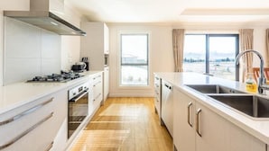 A modern kitchen with white cabinetry, a stainless steel range hood, a built-in oven, and a large window offering a view of a mountainous landscape. - Alpine Star (Lake Tekapo)
