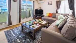 A living room with a sofa, a coffee table with food, a TV, and a balcony with curtains. - Laulea (Kin)