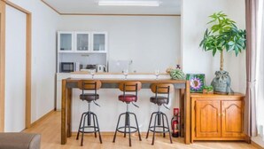 A modern kitchen with a bar area, wooden cabinets, and a potted plant. - Laulea (Kin)