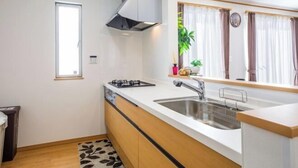 A compact kitchen with a gas stove, two sinks, a window with curtains, and a small plant on the counter. - Laulea (Kin)